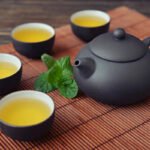 Green tea in cups with mint and teapot on bamboo mat